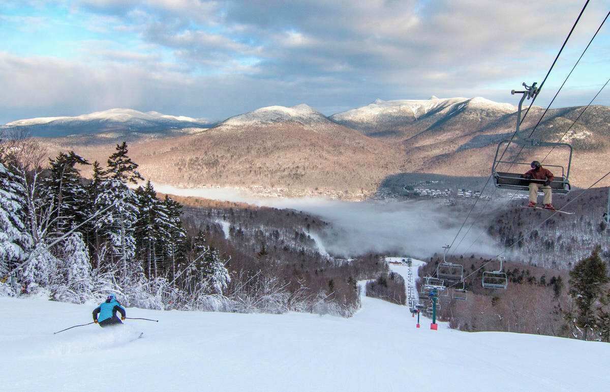 A ski resort with a chairlift, snow-covered trees, and a mountainous backdrop.