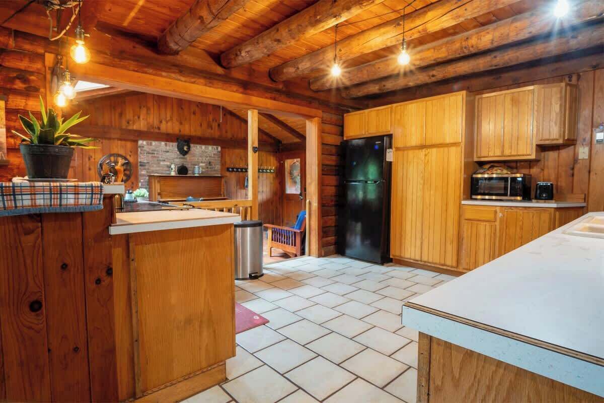 Une cuisine rustique avec des meubles en bois, un réfrigérateur noir et un sol carrelé.