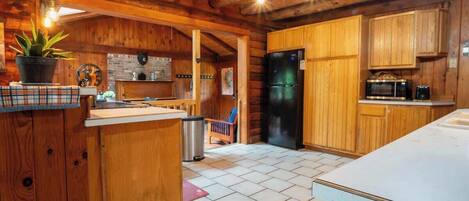 Une cuisine rustique avec des meubles en bois, un réfrigérateur noir et un sol carrelé.