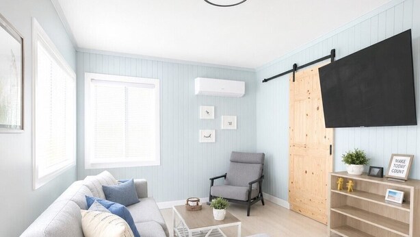 En moderne stue med en grå sofa, et lille bord, en stol og et tv ophængt på væggen.