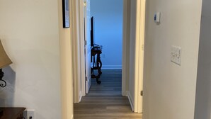 A hallway with wooden flooring, white walls, and a door leading to a room with a blue wall. - 2144 New Bayfront Condo overlooking Mobile Bay (Daphne)