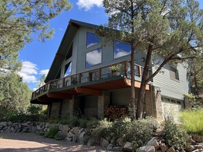 A two-story house with a balcony, surrounded by trees and a stone wall.
