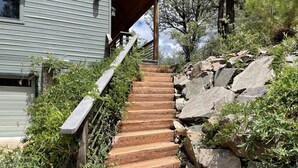Un escalier menant à une maison dont un côté est fait d’un mur de pierre et l’autre d’une terrasse en bois.