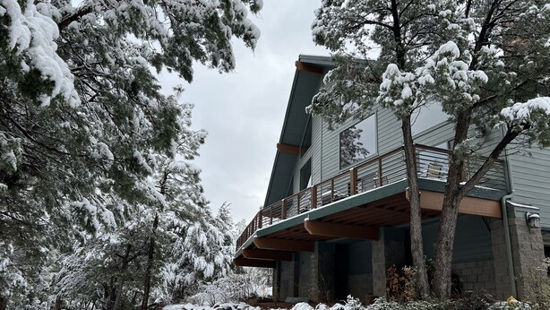 Un bâtiment à deux étages doté d’un balcon, entouré d’arbres couverts de neige et d’un mur de pierre.