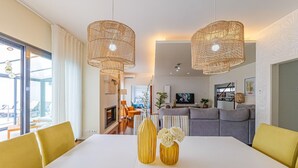 A modern living room with a white sofa, yellow chairs, and a dining table with yellow chairs. There are two large wicker pendant lights hanging from the ceiling. - Villa-4bedroom-3bathroom-pool-petfriendly (Nazaré)