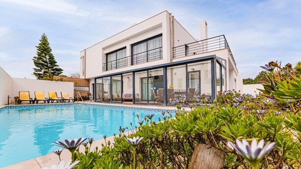 A modern two-story building with a glass-enclosed pool area, outdoor seating, and a balcony. - Villa-4bedroom-3bathroom-pool-petfriendly (Nazaré)