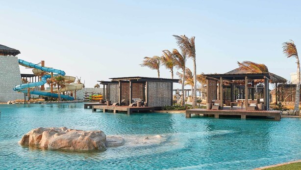 A pool area with a water slide, lounge chairs, and palm trees.