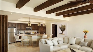 A modern kitchen with dark wooden beams, a central island with bar stools, and a dining area with a light-colored sofa and a coffee table.