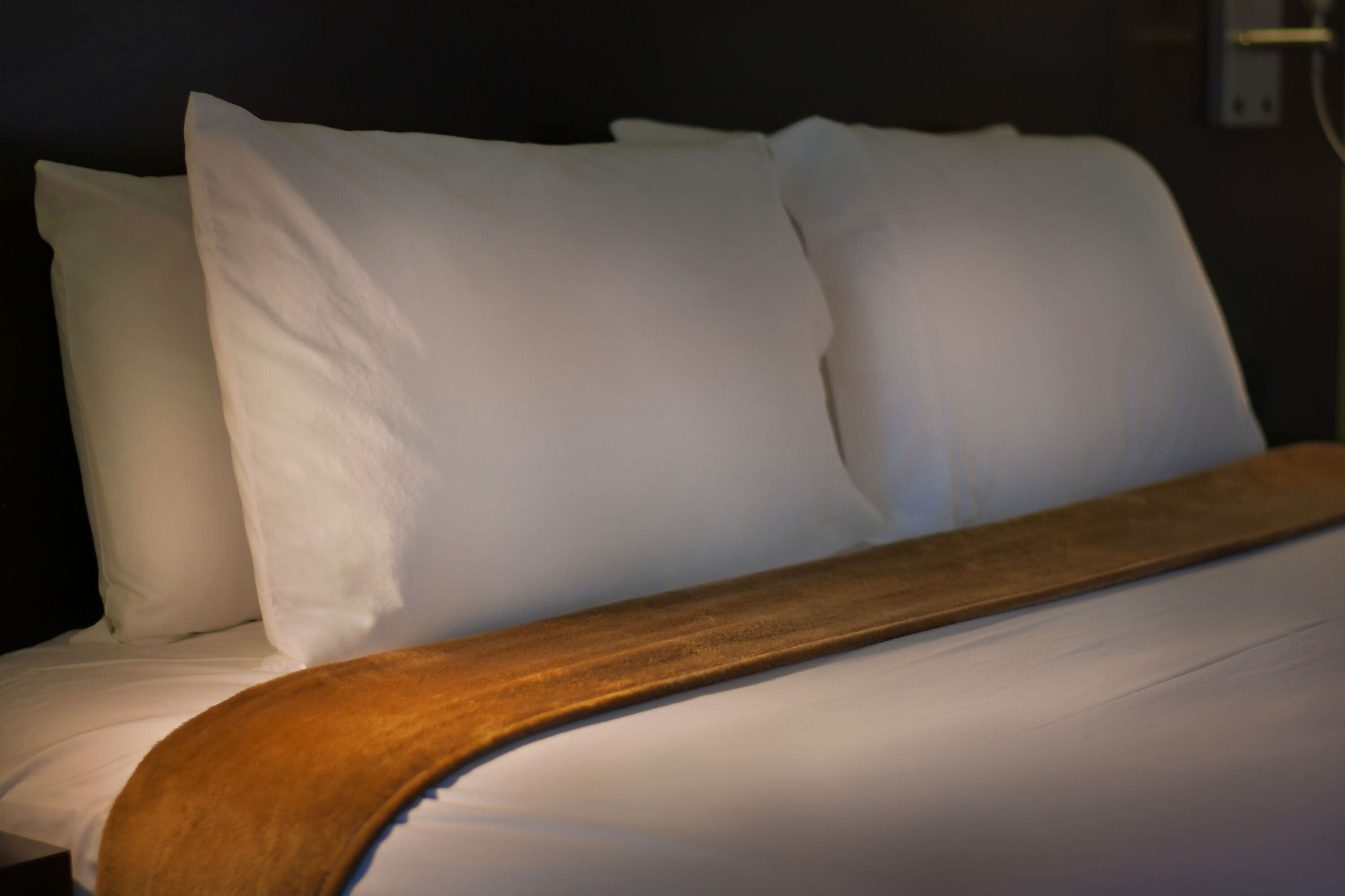 A neatly made bed with white linens and a wooden headboard.