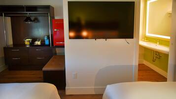 A hotel room with a bed, a TV mounted on the wall, a desk with a red cabinet, and a bathroom with a mirror and sink.