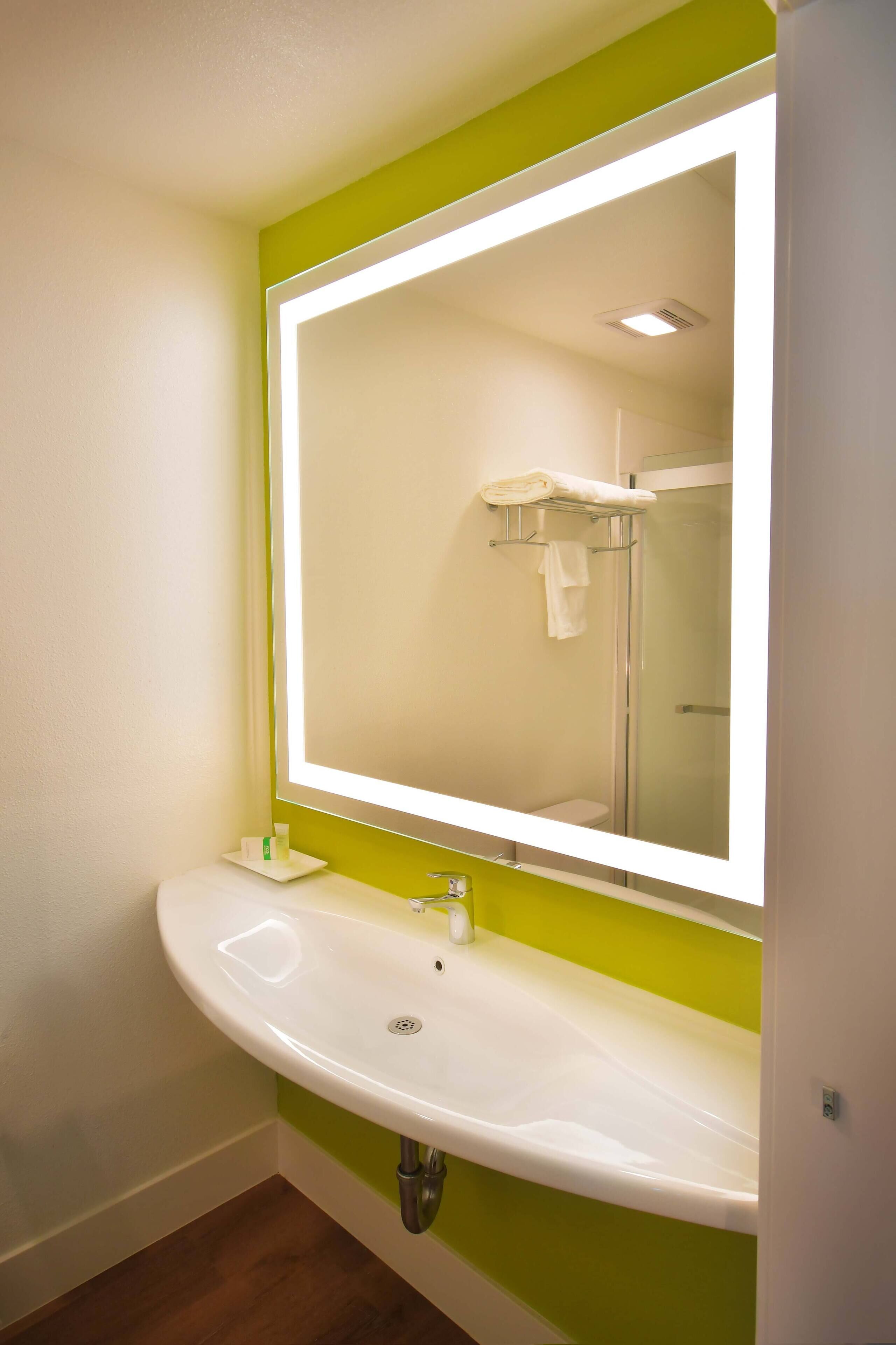 Un baño con un lavabo blanco, paredes verdes y un espejo grande.