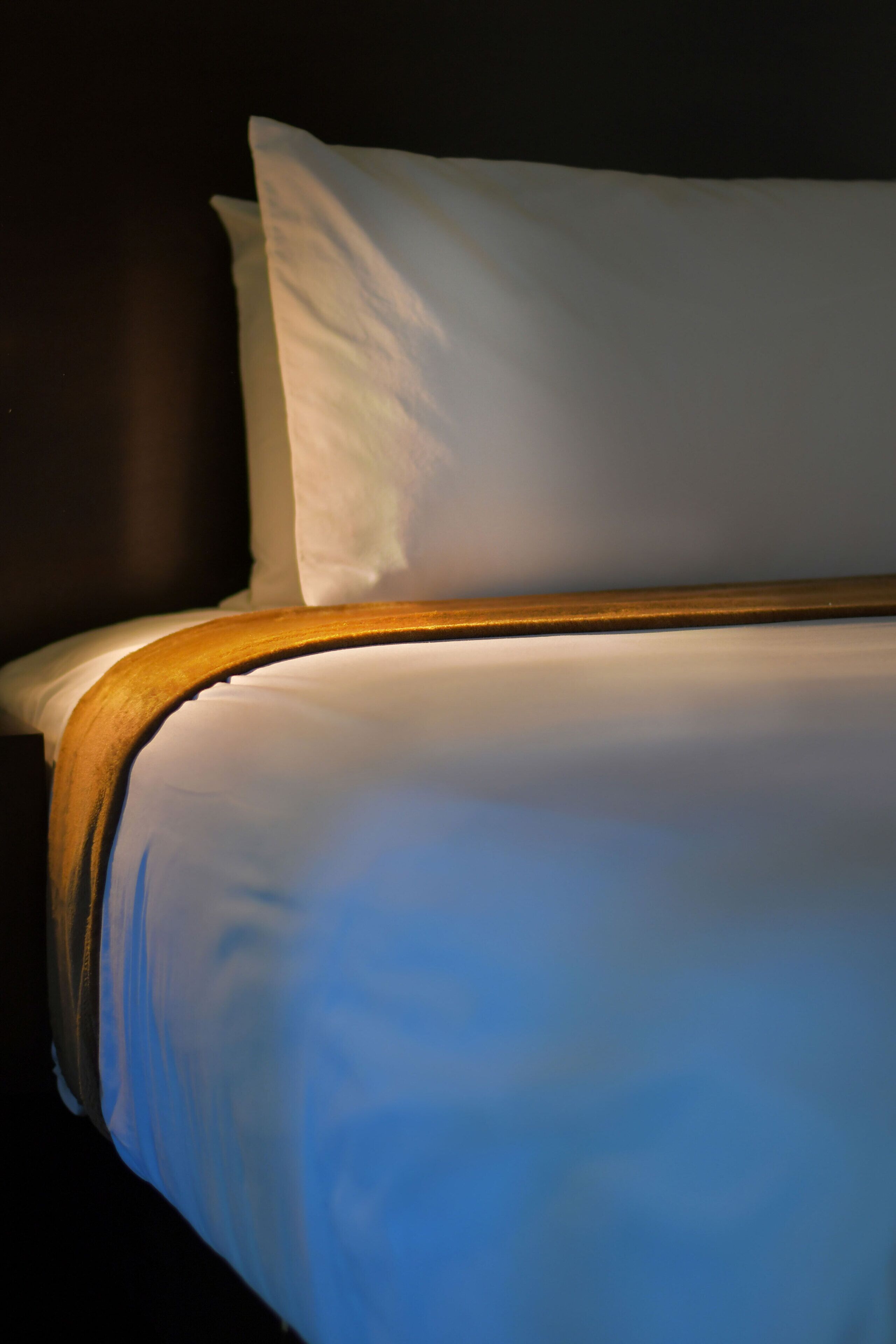 A close-up of a bed with white bedding and a wooden headboard.