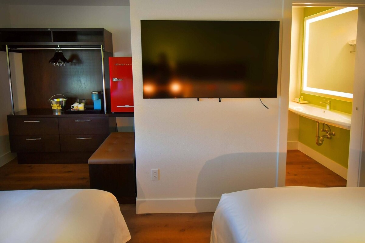 A hotel room with a bed, a TV mounted on the wall, a desk with a red cabinet, and a bathroom with a green wall and a mirror.
