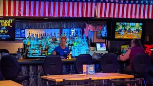 A bar area with a counter, multiple chairs, and a television screen. - The Foothills Motel (Auburn)