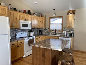 A kitchen with wooden cabinets, a white refrigerator, a microwave, a stove, a sink, and a window with blinds.