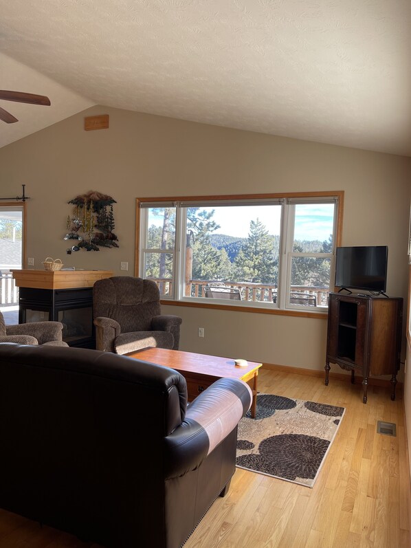 A spacious living room with a large window, a fireplace, a television, and a cozy seating area.