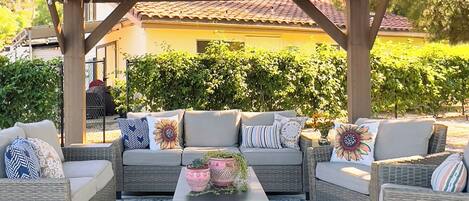 An outdoor seating area with wicker furniture, a patterned rug, and a pergola overhead.