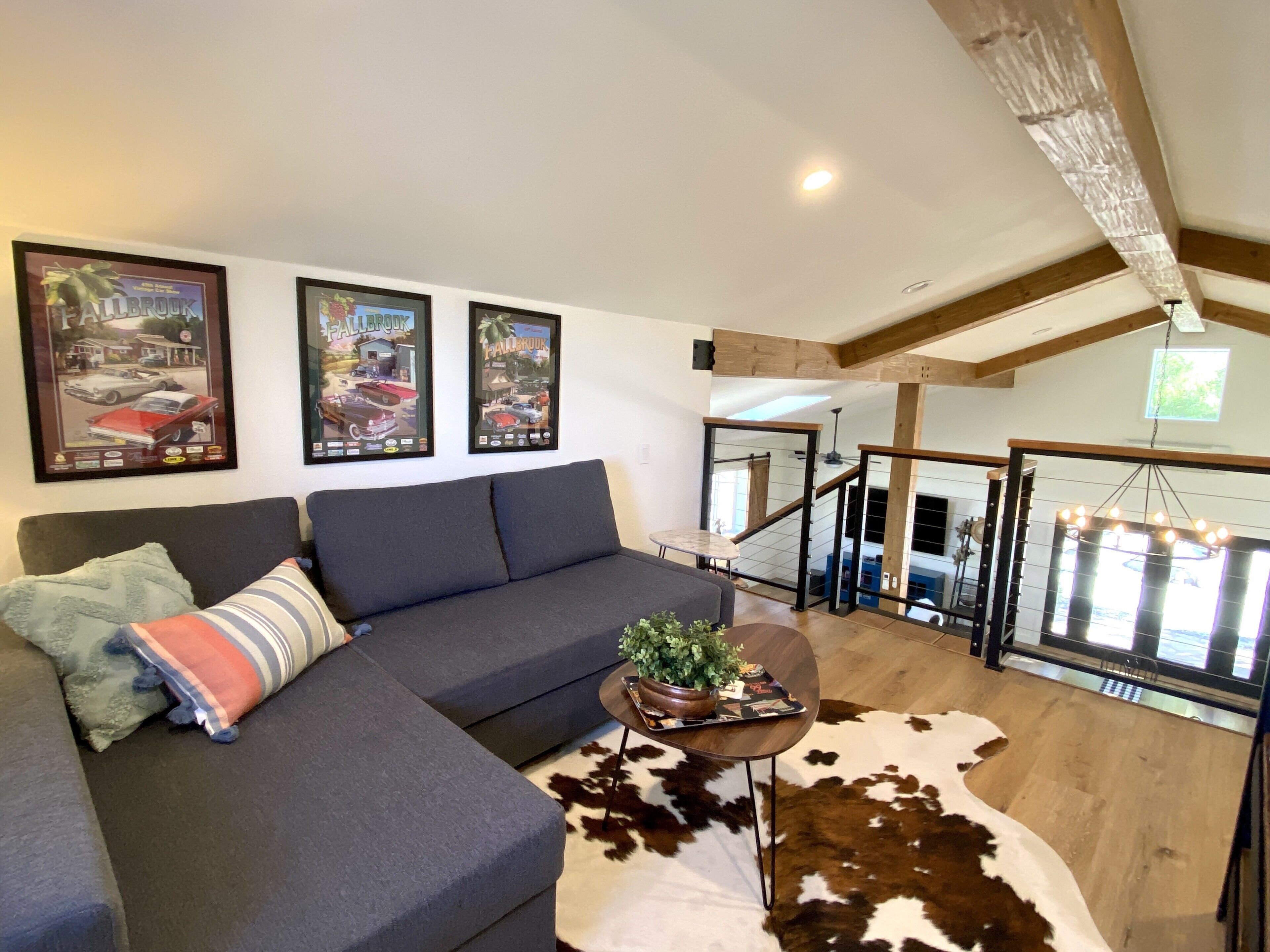 A modern living room with a sectional sofa, a cowhide rug, and framed automotive posters on the wall.