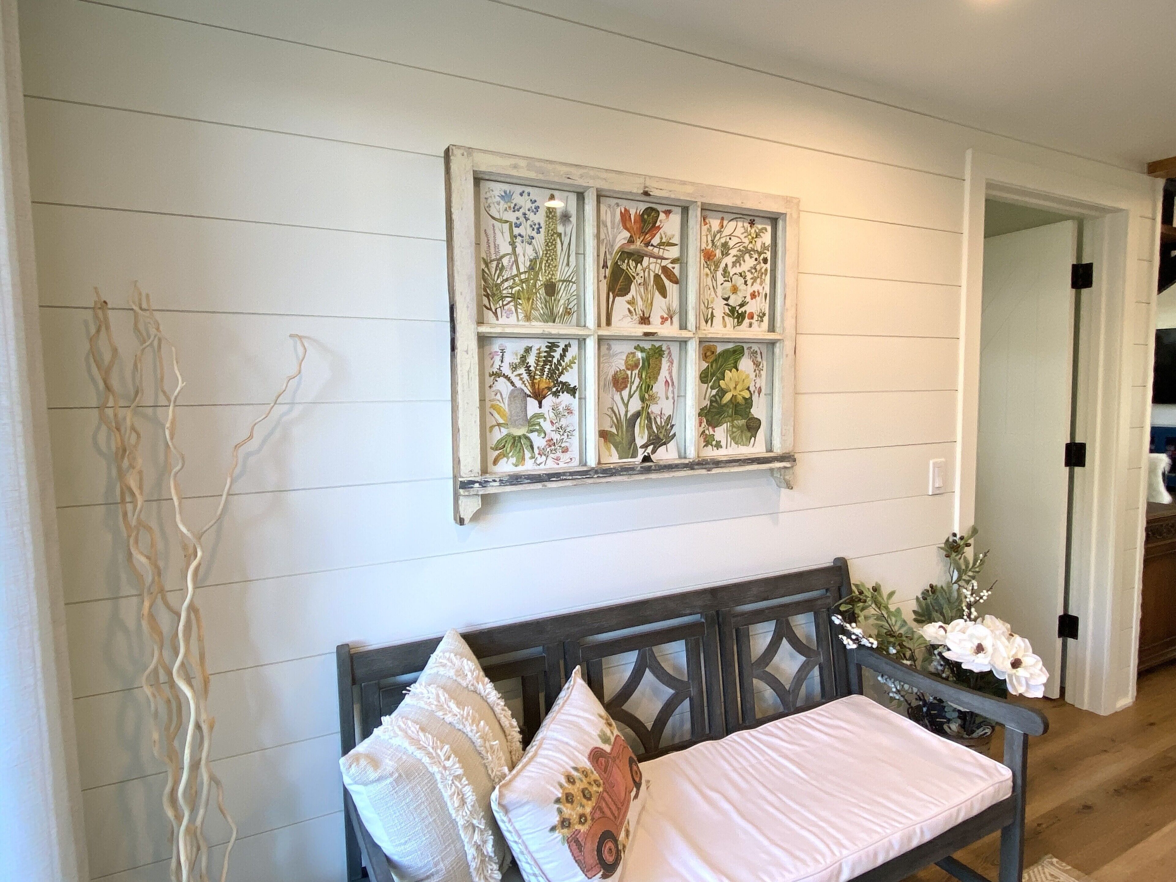 A room with a wooden bench, a wall-mounted botanical print, and a door leading to another room.