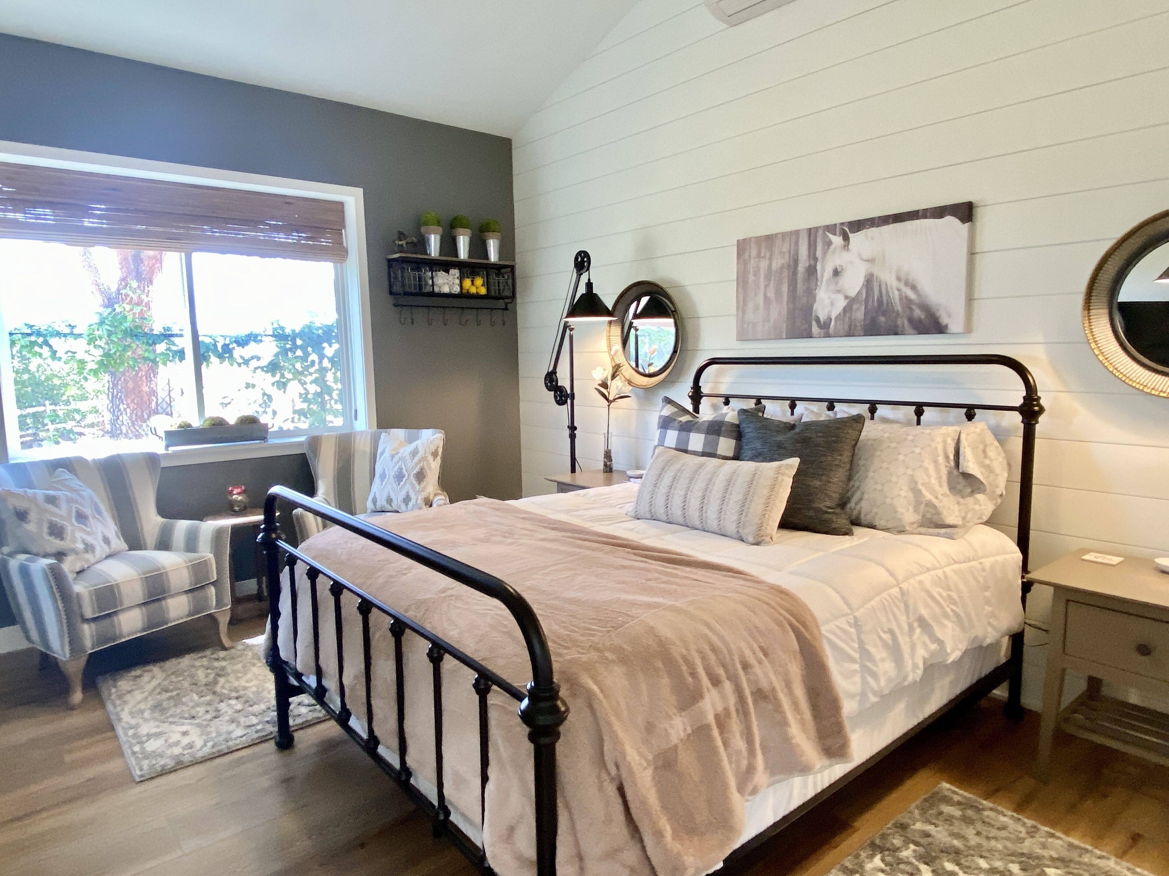 A bedroom with a bed, a chair, a desk, a mirror, and a window.