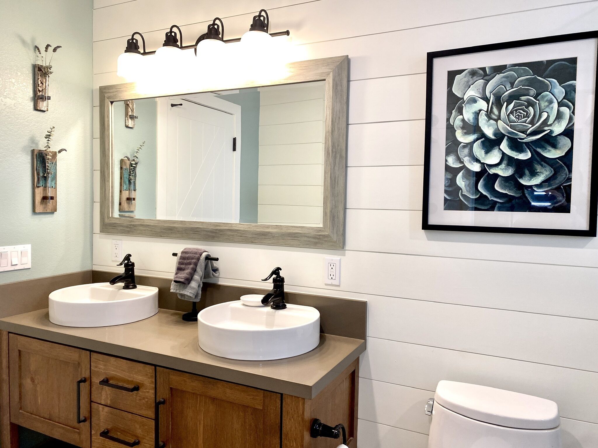 Un bagno con due lavandini, uno specchio, un quadro incorniciato e un water.
