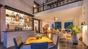 A spacious living area with a wooden dining table, wicker chairs, and a bar area with shelves of bottles. - Casa Jacaranda Hotel Boutique - Cauca Viejo - Mayores de 14 años (Jericó)