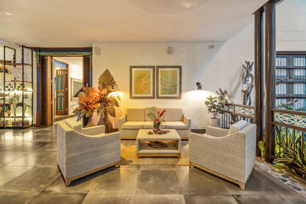 A modern living room with wicker furniture, a coffee table, and a sofa. There are two framed artworks on the wall, a potted plant, and a staircase leading to another level. - Casa Jacaranda Hotel Boutique - Cauca Viejo - Mayores de 14 años (Jericó)
