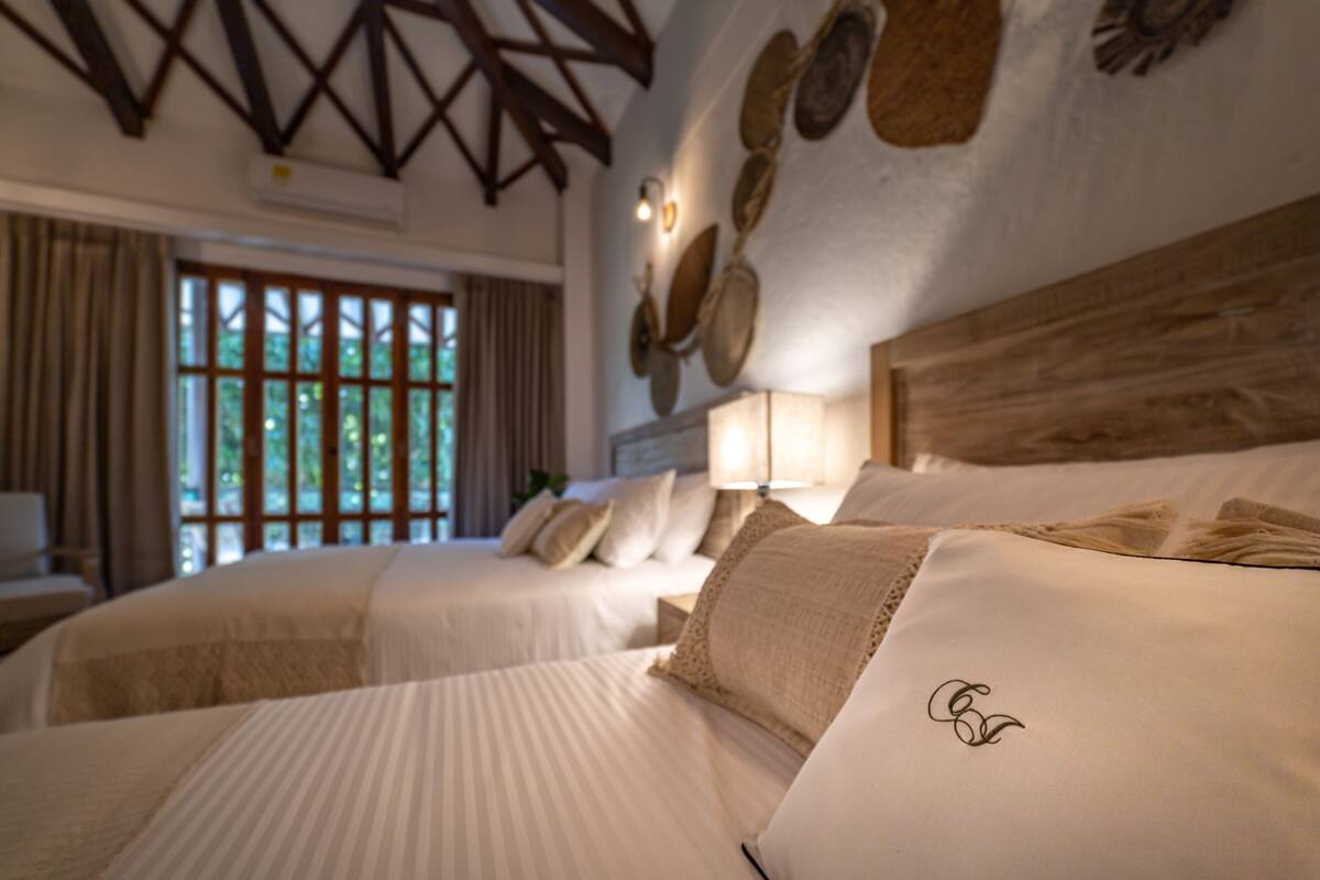 Une chambre d’hôtel avec deux lits, un plafond en bois et une grande fenêtre avec des rideaux.