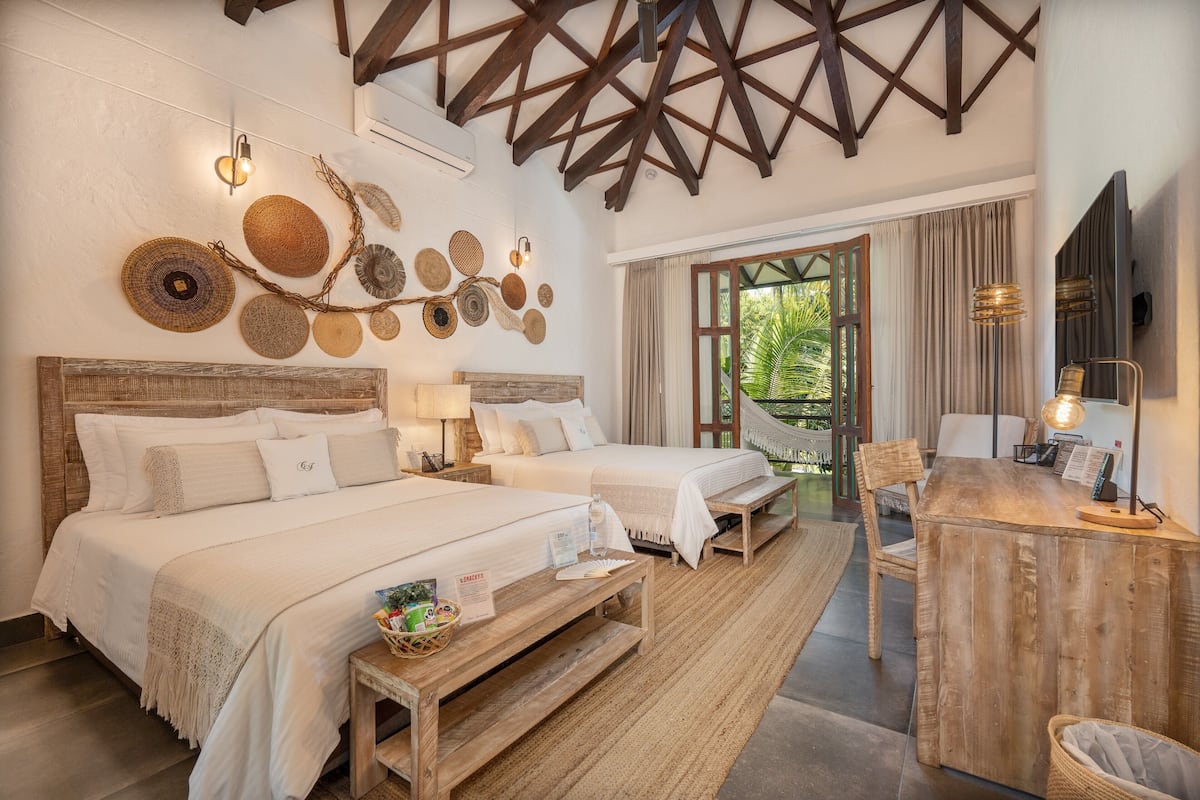 Une chambre d’hôtel avec deux lits, un bureau en bois, une chaise, une télévision et une grande fenêtre donnant sur un paysage verdoyant.