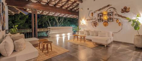 Un vaste espace de vie avec un plafond haut, un canapé blanc, une table basse et une table à manger. On y trouve également des œuvres d’art décoratives accrochées au mur et une grande plante en pot.