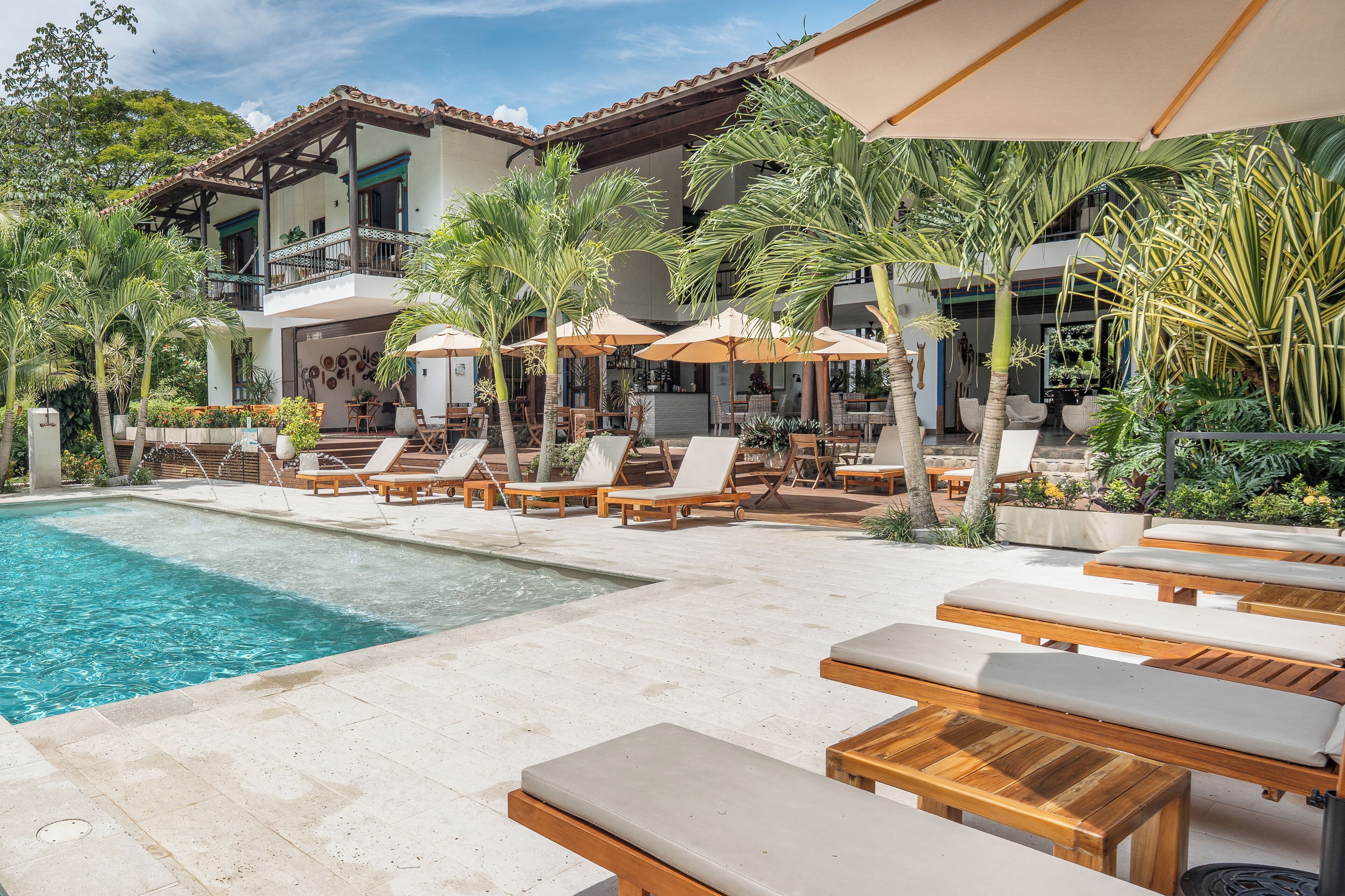 A poolside area with lounge chairs and umbrellas, a clear pool, and a building with a balcony.
