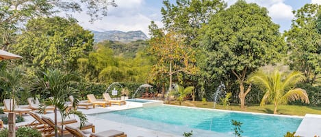 Una piscina al aire libre, sombrillas, sillones reclinables de piscina