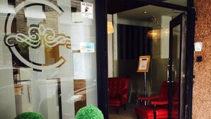A hotel entrance with a glass door, two potted plants, and red chairs inside. - Hotel Cervantes (Mar del Plata)