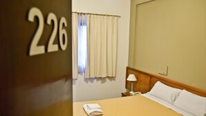 A hotel room with a bed, a nightstand, a lamp, and a window with curtains. - Hotel Cervantes (Mar del Plata)