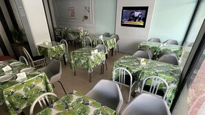 A dining area with tables covered in green tablecloths with tropical leaf patterns, white chairs, and a ceiling fan. - Hotel Cervantes (Mar del Plata)