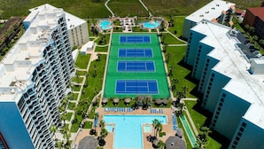Ein Hochhaus-Hotel mit mehreren Tennisplätzen, einem Schwimmbad und Blick auf den Strand.
