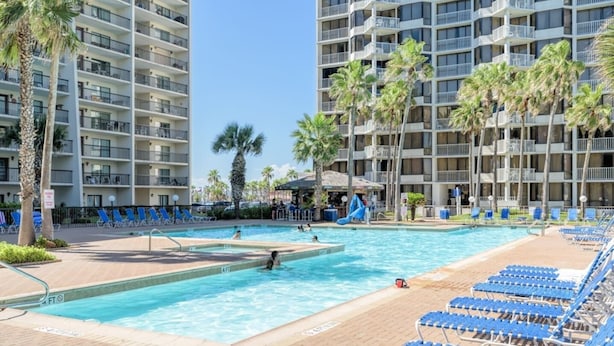 Ein Hotelpoolbereich mit mehreren Balkonebenen, Palmen und blauen Liegestühlen.