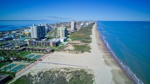 An aerial view of a coastal city with high-rise buildings, a beach, and a sports complex.