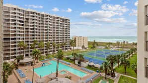 A hotel with a pool, tennis courts, and a view of the ocean.