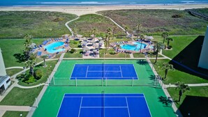 A resort with multiple swimming pools, tennis courts, and a beach view.