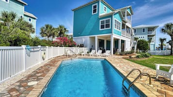 A two-story house with a swimming pool, white fence, and palm trees.