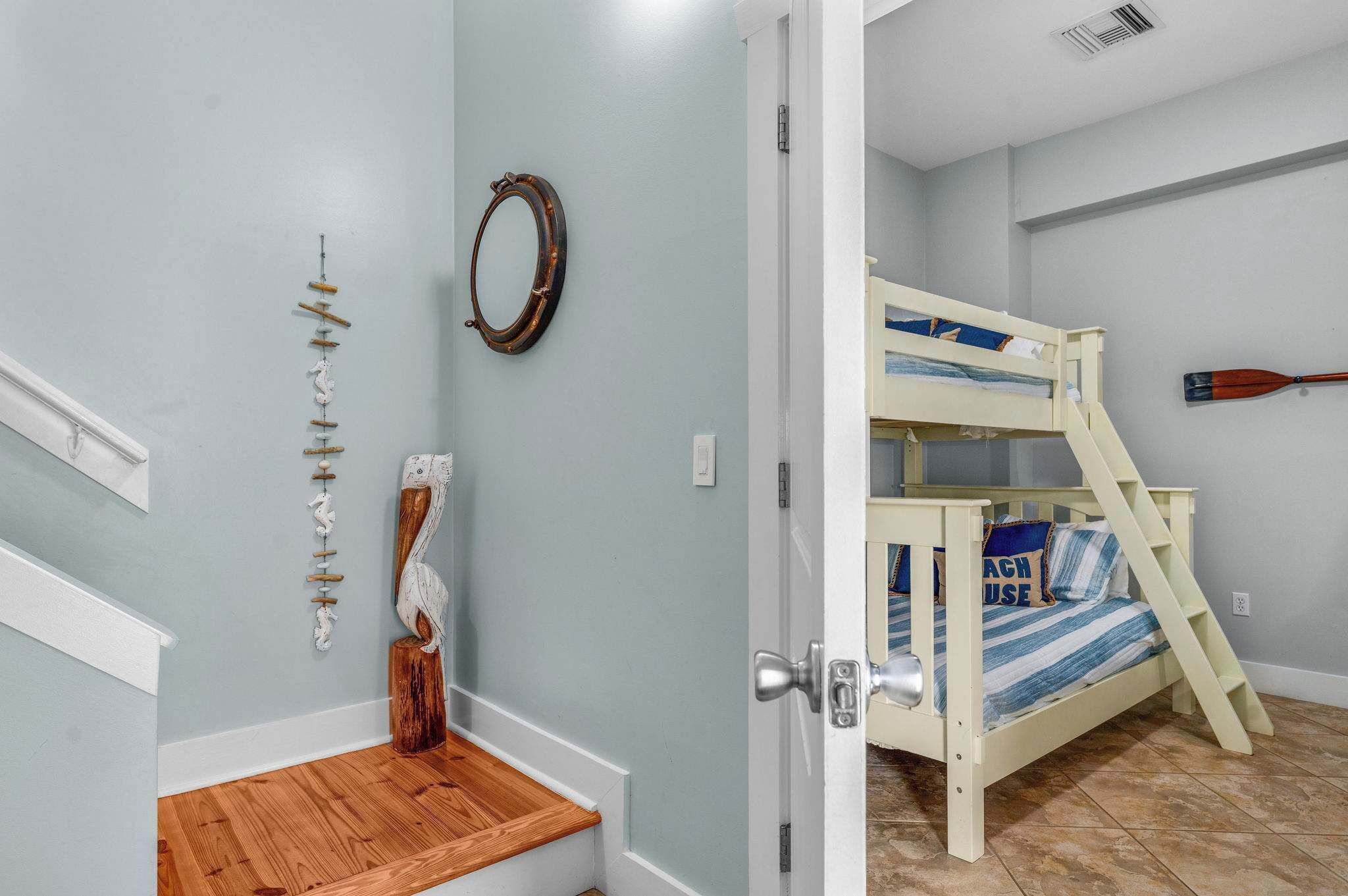 A room with a bunk bed, a wooden bench, a wall-mounted mirror, and a decorative wall piece.