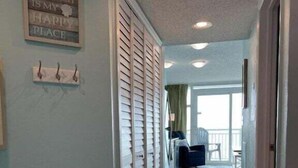 A hallway with a wooden floor, a rug, a sign on the wall, and a door with shutters. - HS-0507 Oceanfront 1-BR Condo in Myrtle Beach, 652 sq ft of coastal comfort for up to 6 guests. (Myrtle Beach)