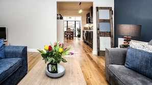 Uma sala de estar moderna com um sofá, uma mesa de centro com um vaso de flores e vista para a cozinha.
