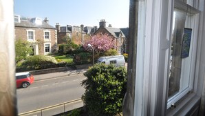 A residential street with houses, a parked van, and a red car. - Central holiday home with pretty, sunny garden, moments from the station, golf course and beach. (North Berwick)
