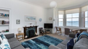 A living room with a fireplace, a television, and a view of the sea. - Lovely beachside apartment, with uninterrupted views across to the Fife coastline.  Sleeps 8. (North Berwick)