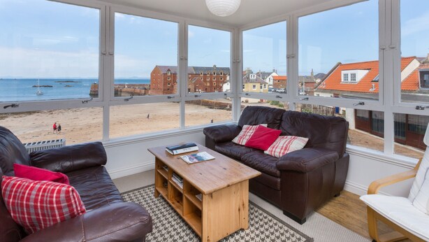 A room with large windows overlooking a beach, furnished with leather sofas and a wooden coffee table. - Lovely beachside apartment, with uninterrupted views across to the Fife coastline.  Sleeps 8. (North Berwick)