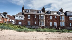 A row of brick houses with multiple windows and a sandy foreground. - Lovely beachside apartment, with uninterrupted views across to the Fife coastline.  Sleeps 8. (North Berwick)