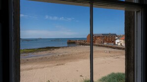 A beach view from a window with a clear sky, a sandy beach, and buildings in the background. - Lovely beachside apartment, with uninterrupted views across to the Fife coastline.  Sleeps 8. (North Berwick)