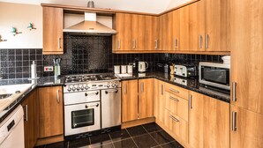 A kitchen with wooden cabinets, a stove, oven, microwave, and a sink. - A delightful, homely cottage.  A great base for all of East Lothian. Sleeps 4. (Gullane)